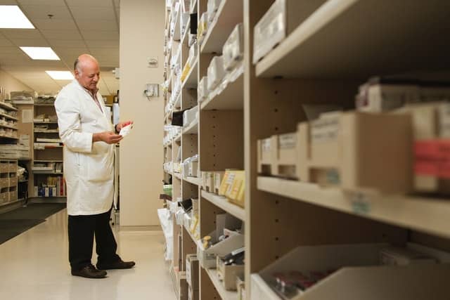 A man in a white lab coat looking at shelves of medication