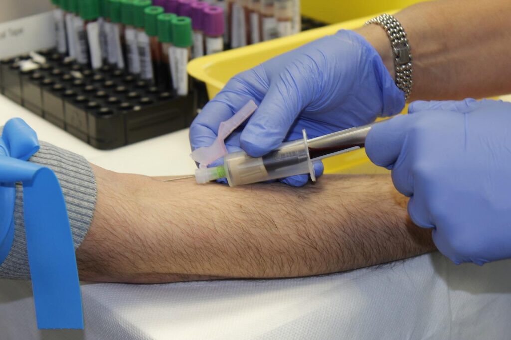 A phlebotomist wearing blue gloves drawing blood from a patient who has a tourniquet on